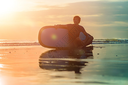 日落时与冲浪板一起坐在海滨海滩的冲浪男子的休眠假期活力男生活动木板海岸乐趣日出海岸线运动图片