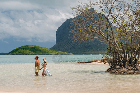 毛里求斯岛莫纳山背景下 泳装少女和短裤男站在海中太阳喷射天空海岸海洋海滩假期女士旅行家庭图片