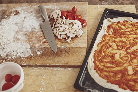 木板上配有披萨和附近蘑菇及番茄的烤盘图片