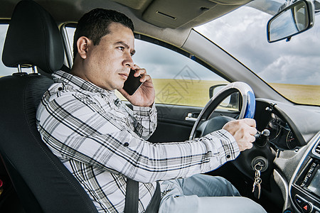 一个男司机在他的车里打电话 一个男人在开车时打电话的概念 一个年轻人坐在车里用手机的侧视图图片