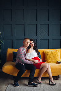 坐在黄色沙发上看摄影机的一对时髦夫妇图片