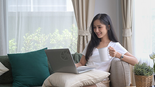 身居沙发 使用笔记本电脑 上网 检查电子邮件的年轻女性图片