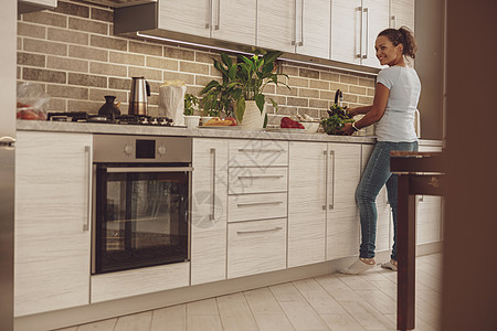 一个女人洗绿菜做沙拉 站在水槽前面厨房的厨房里图片