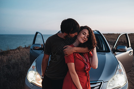 在日落后海边的SUV汽车旁抱抱和接吻 爱人共度欢乐时光 双情侣图片