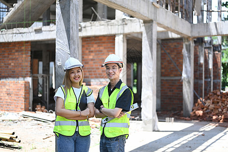 两名年轻的工程师站立建筑工地 对摄影机微笑图片