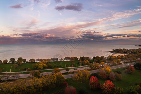 在芝加哥的密歇根湖和湖岸大道上 秋天日落美丽 有粉红色和蓝色云雾 还有红黄绿树叶图片