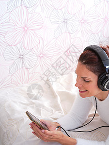 使用手机和听音乐躺在床上的女人图片