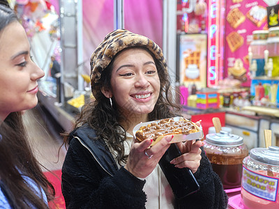 穿着帽子笑着拉蒂娜女人 在夜展中吃巧克力华夫饼图片