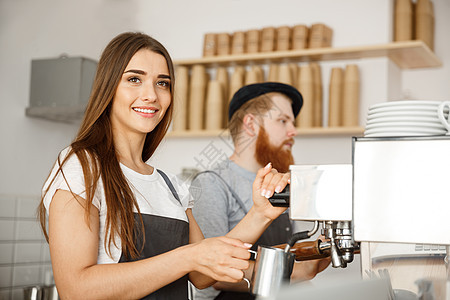 咖啡业务概念站在咖啡馆时 女咖啡师穿着围裙准备和蒸牛奶 与她的伴侣一起点咖啡餐厅机器投手职业女士棍棒男性工作服务员咖啡店图片