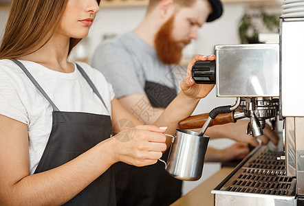 咖啡业务概念站在咖啡馆时 女咖啡师穿着围裙准备和蒸牛奶 与她的伴侣一起点咖啡职业女士服务咖啡机餐饮女孩员工女性投手制作者图片