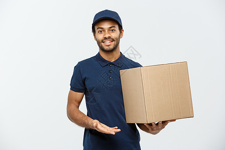 送货概念快乐的非洲裔美国送货员的肖像 指着手展示一个盒子包裹 隔绝在灰色演播室背景 复制空间手指导游微笑船运白色成人男生服务男性图片