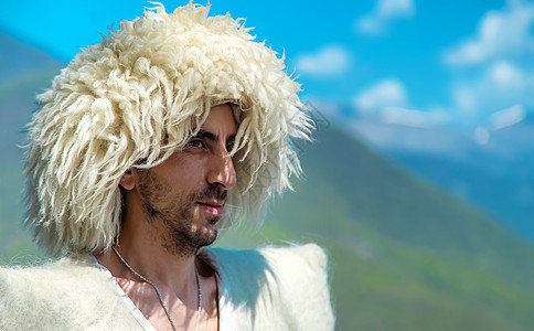 一个身戴帽子的格鲁吉亚人 在山顶和天空的背景之下 有选择地专注横幅传统毛皮牧羊人文化太阳裙子披风木瓜羊毛图片