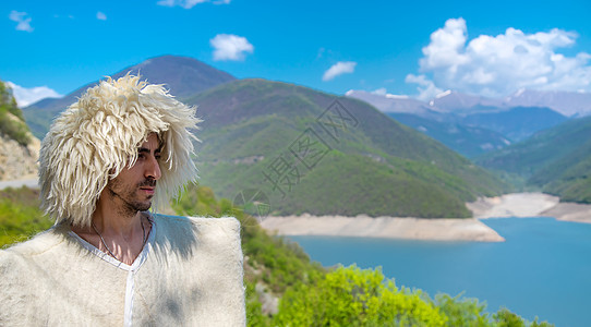 一个身戴帽子的格鲁吉亚人 在山顶和天空的背景之下 有选择地专注木瓜衣服披风毛皮纪念品景点国家头饰羊毛横幅图片