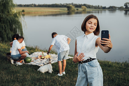 白人女孩在户外湖边家庭亲身经历水风浪事件时 在智能手机上做自拍图片