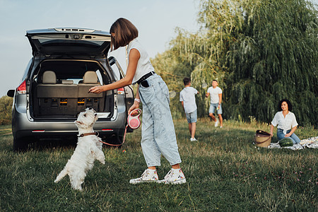 在Minivan Car的公路旅行中与西高地白人三角狗一起玩耍 讨论她家庭在迷你车路上有乐趣出家门的背景父亲女儿孩子们青少年高地图片