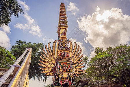 印度尼西亚巴厘岛乌布德市中央街道上 传统恶魔的拜林树雕塑和鲜花组成的巴德火化塔 为即将到来的火化仪式做准备信仰偶像监护人天空衣服图片