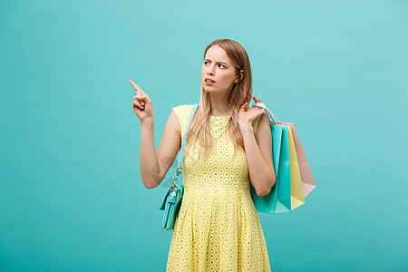 穿着愤怒的身着衣服的女孩在蓝背景上被孤立 持有购物纸袋供取走和指手指广告女朋友工作室成人手势商务女性送货食物工艺图片