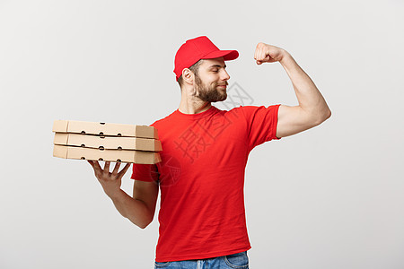 交付概念强健英俊送货员的肖像 他伸展肌肉并拿着披萨盒包 孤立在灰色工作室背景上 复制空间男人商业胡须男性服务纸板展示邮递员食物微图片