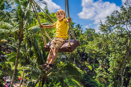 小男孩在印度尼西亚巴厘岛的丛林雨林中荡秋千 在热带摇摆 秋千  巴厘岛的趋势 带着孩子旅行的概念 带孩子怎么办 儿童友好的地方悬图片