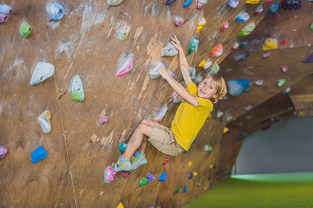 小男孩穿特别靴子在石墙上爬挑战风险男人运动岩石童年齿轮安全头盔训练图片