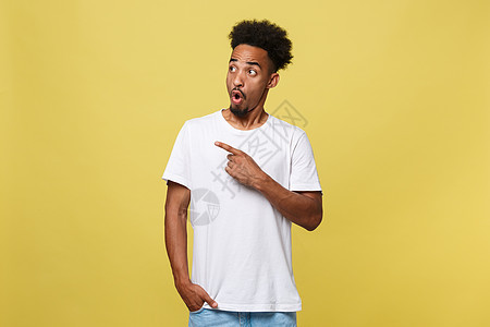 照片中 年轻的非洲裔美国男子在室内照片中被孤立在灰色背景中 他指着他的白色空白 T 恤 吸引人们注意上面的广告 推销商品 应用程图片