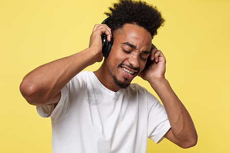 有耳机的有吸引力的非裔美国人听音乐 在黄色金色背景上孤立无援舞蹈闲暇男人衬衫技术黑色享受音乐白色男性图片