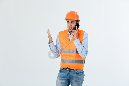 建筑工程师在移动电话上讲话 严重成年男子使用智能手机与建筑工地工人进行沟通 单位 千分之五项目导师领班工程安全帽技术建筑师员工男图片