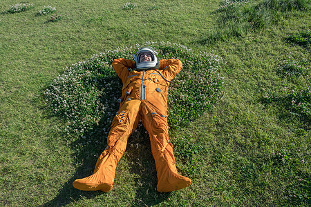 穿着太空服和头盔在户外绿色草地上休息的快乐宇航员图片