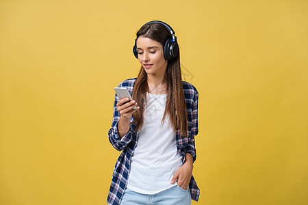 在耳机中听音乐和歌唱黄色背景的美丽的年轻女青春女子工具女士手机收音机技术享受旋律表演唱歌闲暇图片