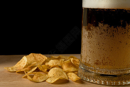 在木板和黑色背景上装着啤酒和薯片的玻璃杯饮料茶点酒吧土豆玻璃派对桌子脂肪盘子筹码图片