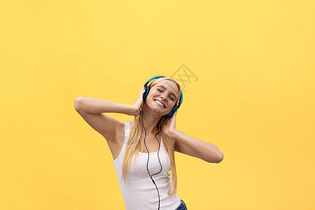 生活方式概念 一个穿着白色T恤衫的欢乐女人的肖像 用耳机听音乐 同时在黄色背景中单独跳舞和唱歌女孩青年女性享受成人微笑娱乐电话手图片