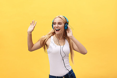 生活方式概念 一个穿着白色T恤衫的欢乐女人的肖像 用耳机听音乐 同时在黄色背景中单独跳舞和唱歌青年手机技术幸福娱乐歌曲女士享受闲图片