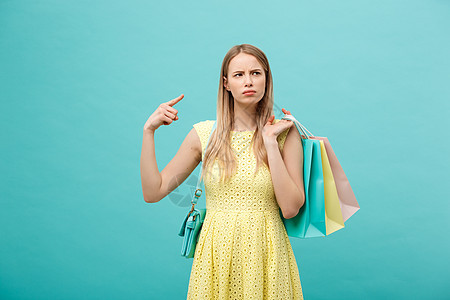 穿着愤怒的身着衣服的女孩在蓝背景上被孤立 持有购物纸袋供取走和指手指手势青年女性送货女士命令食物广告工艺工作室图片