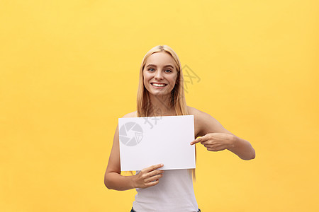 黄色背景的年轻女性持有空白纸页 并用手指复制空间来表示惊喜表达方式 笑声展示微笑手势卷发成人震惊女士信仰床单合同图片