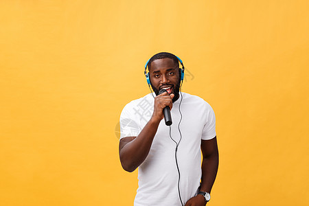 欢快积极 别致 英俊的非洲男子手持麦克风 头戴耳机听音乐唱歌 享受黄色背景中孤立的周末假期的肖像音乐播放器乐趣工具寒意女孩男人男图片