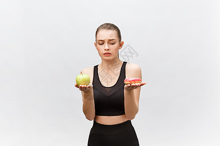 年轻女性在白种背景上选择甜甜圈和苹果 饮食概念女孩女士肥胖减肥重量营养动机损失身体运动图片