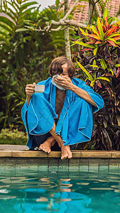生病的旅行者 男人在度假时感冒了 伤心地坐在泳池边喝茶 用餐巾纸擤鼻涕 他的儿子很健康 正在游泳池里游泳 Instagram 移图片