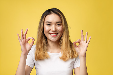 亚裔年轻女性手势良好 在黄色背景上被孤立女士衬衫微笑成功手指人士工作室成人球座女孩图片