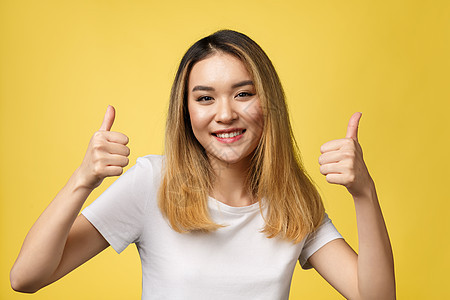 年轻亚洲女性在黄色背景上露出拇指快乐手指成人衬衫微笑女士工作室手势展示女孩图片