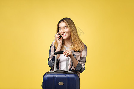 快乐的亚洲女性旅行者的画像 带着手提箱 在孤立的黄色背景下看着手机女士人士电话背包白色旅行牛仔裤行李女孩商务图片