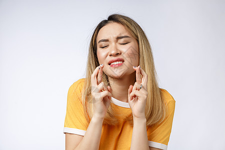 身穿便衣的年轻女性祈祷求神 请抬头看着她用手指穿过灰色背景时所隔绝的一丝不挂女孩黑发白色快乐欲望微笑焦虑运气情绪手势图片