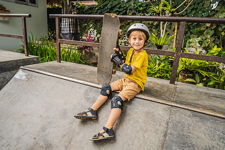 戴头盔和膝盖垫的体育男孩学会在滑板公园与滑板一起玩滑板木板乐趣溜冰者滑冰潮人青年平衡学习孩子城市图片