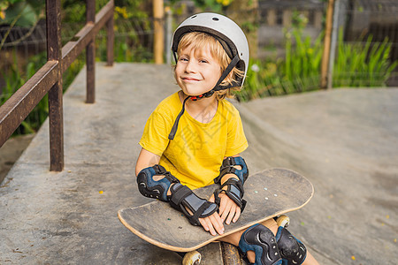 戴头盔和膝盖垫的体育男孩学会在滑板公园与滑板一起玩滑板长板快乐城市童年孩子滑冰街道公园男性男生图片