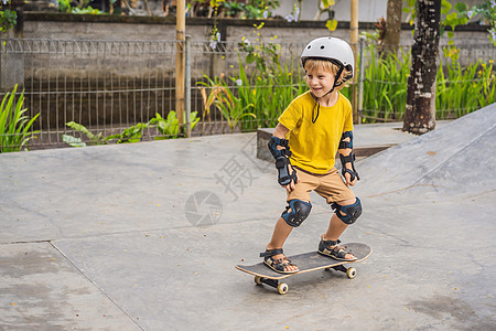 戴头盔和膝盖垫的体育男孩学会在滑板公园与滑板一起玩滑板娱乐童年运动鞋男性城市生活长板滑冰木板快乐孩子图片