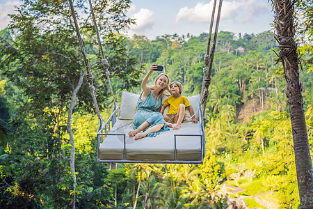 母亲和儿子在印度尼西亚巴厘岛的丛林雨林中荡秋千 在热带摇摆 秋千  巴厘岛的趋势 带着孩子旅行的概念 带孩子怎么办 儿童友好的地图片