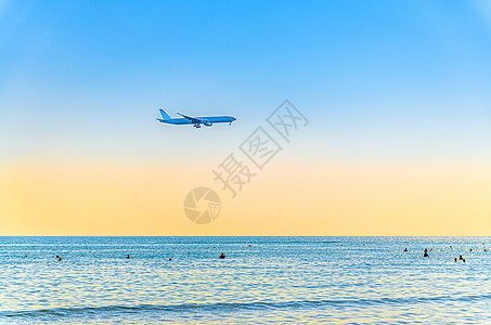 飞机在海面上低空飞行 游客在水中游泳 日落时清澈的蓝橙色天空 飞机准备降落运输蓝色海岸土地地平线假期翅膀旅行方法航空图片