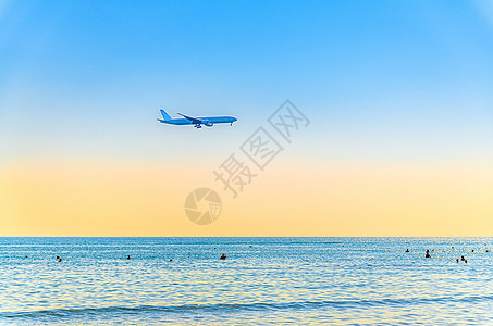 飞机在海面上低空飞行 游客在水中游泳 日落时清澈的蓝橙色天空 飞机准备降落运输蓝色海岸土地地平线假期翅膀旅行方法航空图片