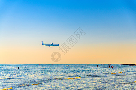 飞机在海面上低空飞行 游客在水中游泳 日落时清澈的蓝橙色天空 飞机准备降落喷射速度运输飞机场海岸假期翅膀空气旅行车辆图片