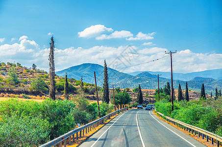塞浦路斯地貌景观 车辆在河谷的沥青路上行驶 有黄色干燥田 树和路边杆土地曲线农村风景蓝色汽车骑术旅行两极天空图片