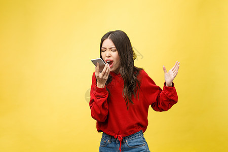 愤怒的年轻亚洲女性在黄色背景上站立时 在手机上失望 但身处黄底商业压力商务人士技术尖叫讲话细胞挫折女孩图片
